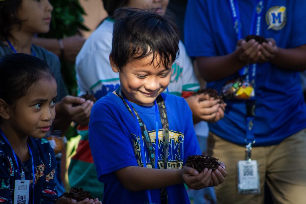 Young boy smiles down at a small pile of mulch he holds in his hands