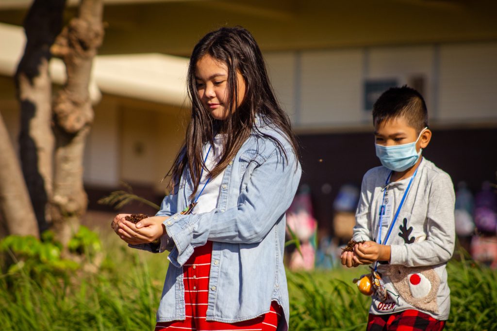 two keiki carry small piles of mulch in their hands