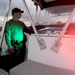 Picture taken from the bow of a DOCARE marine patrol boat on Kāne‘ohe Bay sandbar at dusk. DOCARE officer stands near the helm with the boat's bright green and red lights on and the bay waters and overcast sky in the background, 01-07-2022.