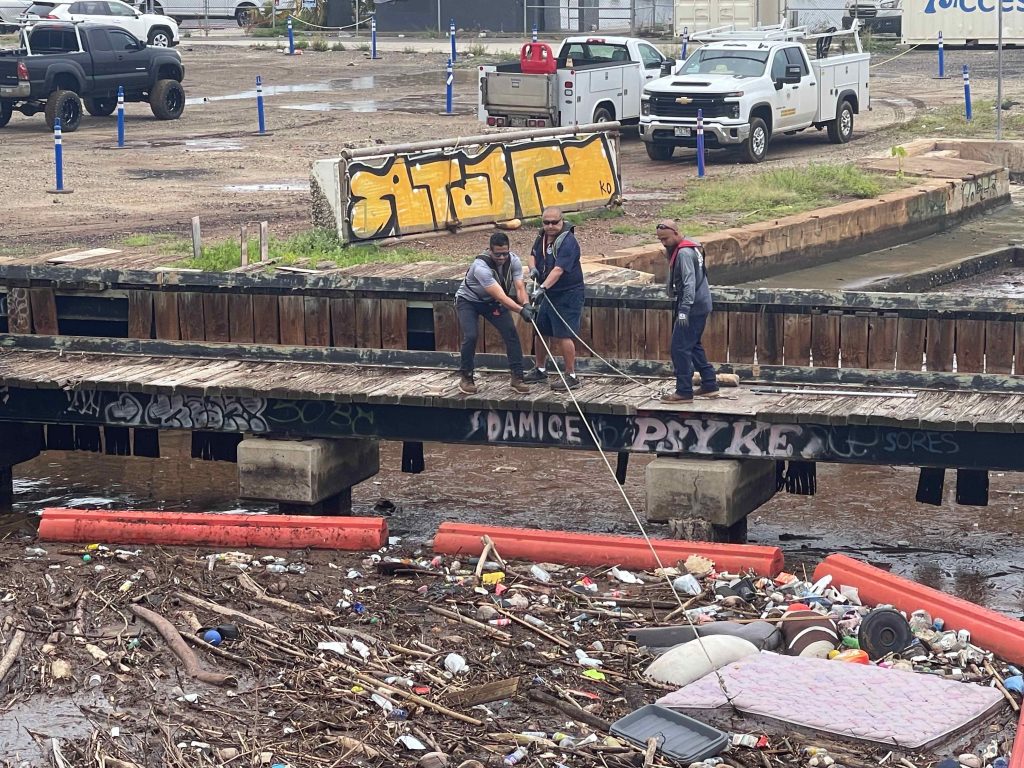 Department of Land and Natural Resources’ Division of Boating and Ocean Recreation crew members on a pier over the Ala Wai Canal use a rope and hook to pull a large mattress out of the water, 03-15-2026.